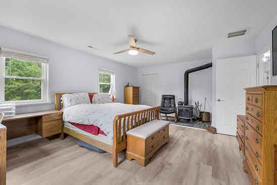 Primary bedroom at 1701 Harrington Road, Orange VA, featuring wood floors, natural light, ceiling fan, and a wood stove in the corner.