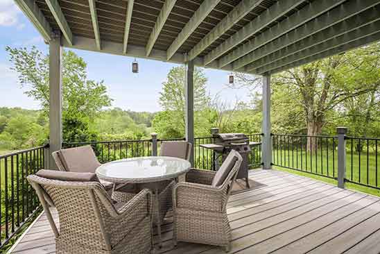 Covered deck at 1701 Harrington Road, Orange VA, featuring outdoor dining set, grill, and scenic views of trees and open lawn.