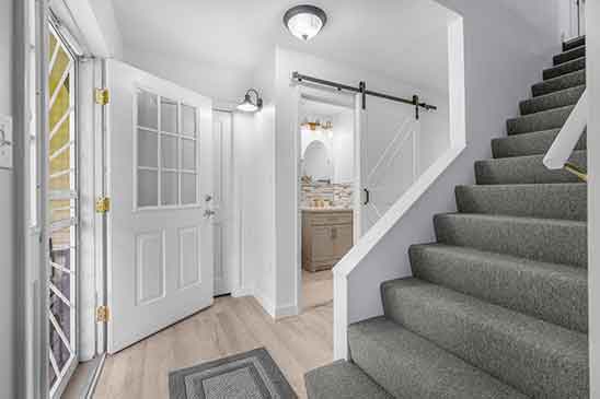 Bright entryway at 1701 Harrington Road, Orange VA, featuring a staircase with gray carpet, open doorway, light wood flooring, and sliding barn door to bathroom.