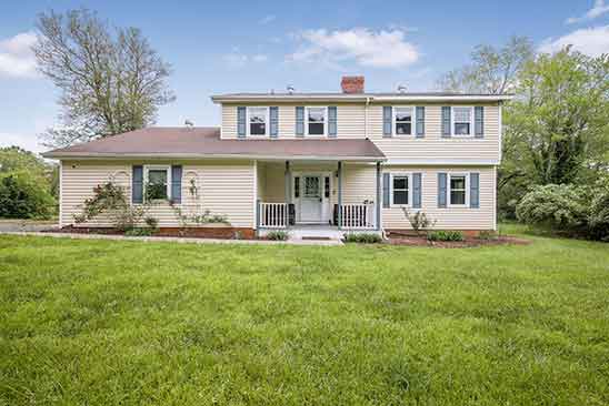 Front view of the renovated farmhouse at 1701 Harrington Road in Orange, Virginia, featuring classic siding, a covered front porch, and manicured lawn.
