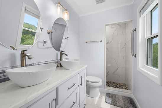 Modern bathroom at 1701 Harrington Road, Orange VA, with dual vessel sinks, marble-tile shower, round mirrors, and natural light.