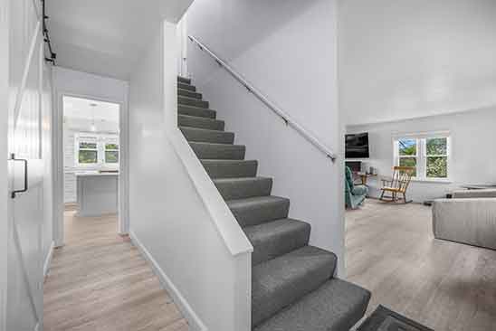 Bright interior view at 1701 Harrington Road, Orange VA, showing staircase, open living room, light wood floors, and kitchen entrance in the background.
