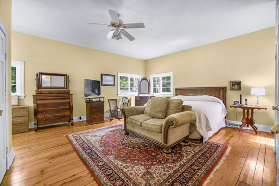 Primary bedroom at 3665 Old River Trail in Powhatan, Virginia, featuring heart pine floors, large windows, and a seating area. This spacious suite at Pleasant Oak includes an en suite bath and opens to a private garden patio.
