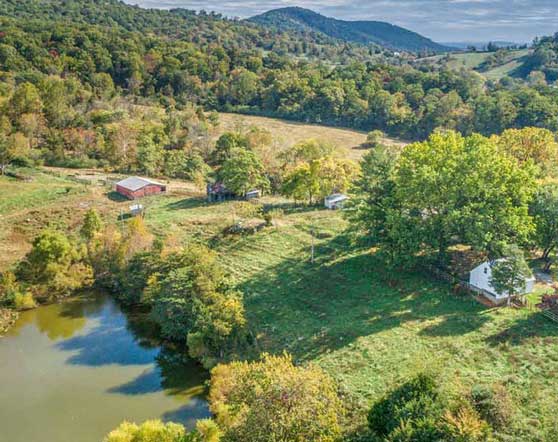 Charming historic farmhouse with white siding, a rustic metal roof, and a prominent stone chimney, nestled among mature trees. The home exudes country charm with its timeless architecture and tranquil rural setting. Sold